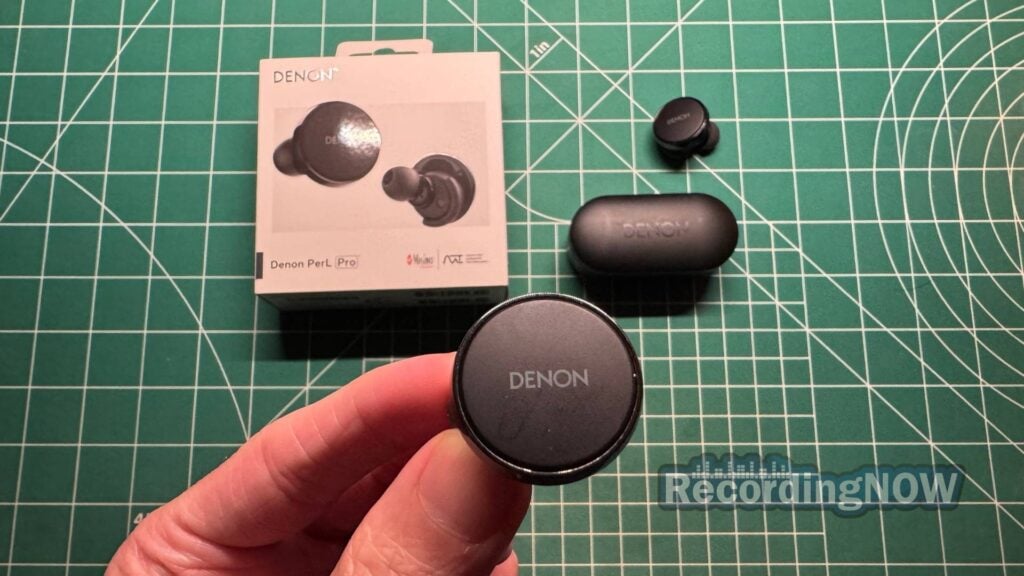 Holding Denon PerL Pro wireless earbud next to charging case and original box packaging