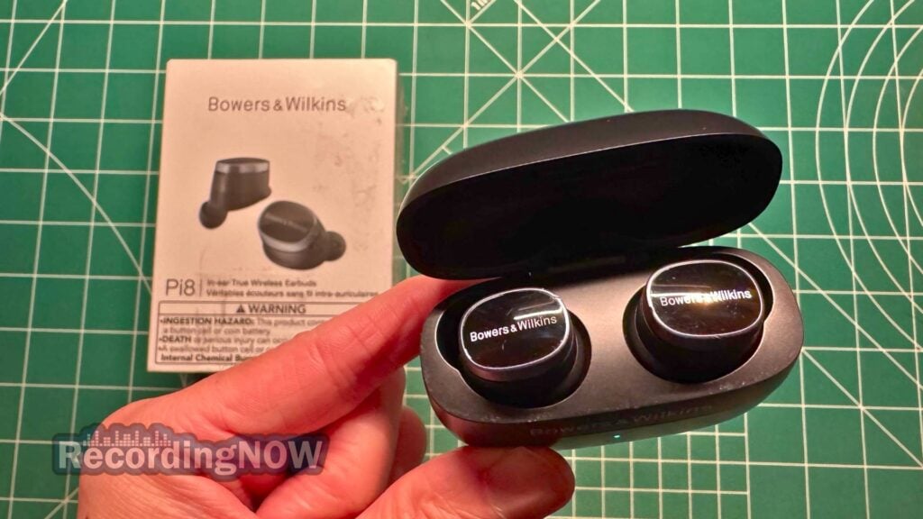 Holding Bowers and Wilkins Pi8 wireless earbuds inside charging case next to original box packaging
